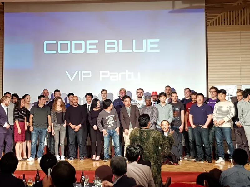 Gruppenfoto vieler Teilnehmender auf einer Bühne vor der Leinwand „Code Blue – VIP Party“.